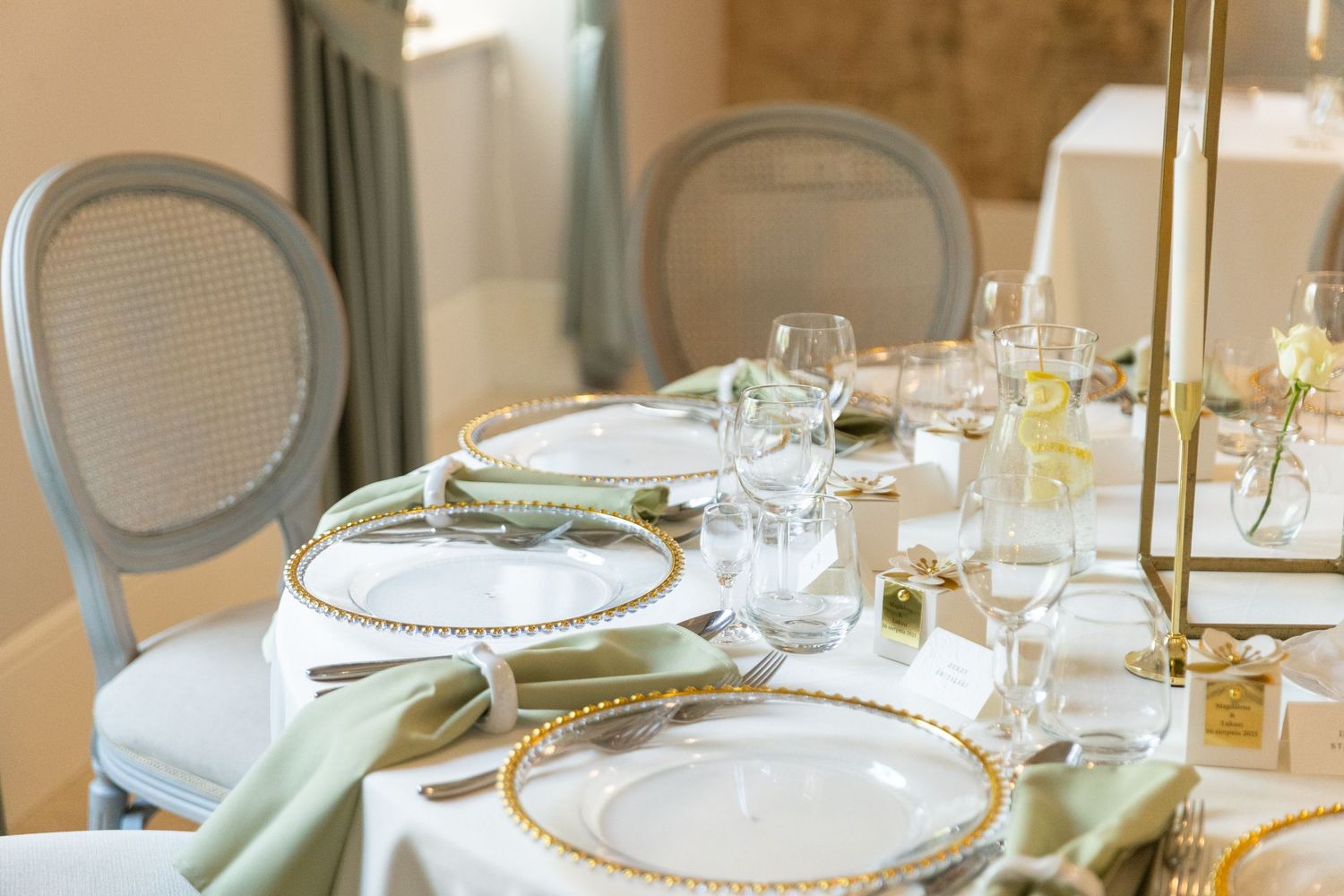 Elegant table settings with white plates, glassware, and soft green accents in a bright dining room setting.