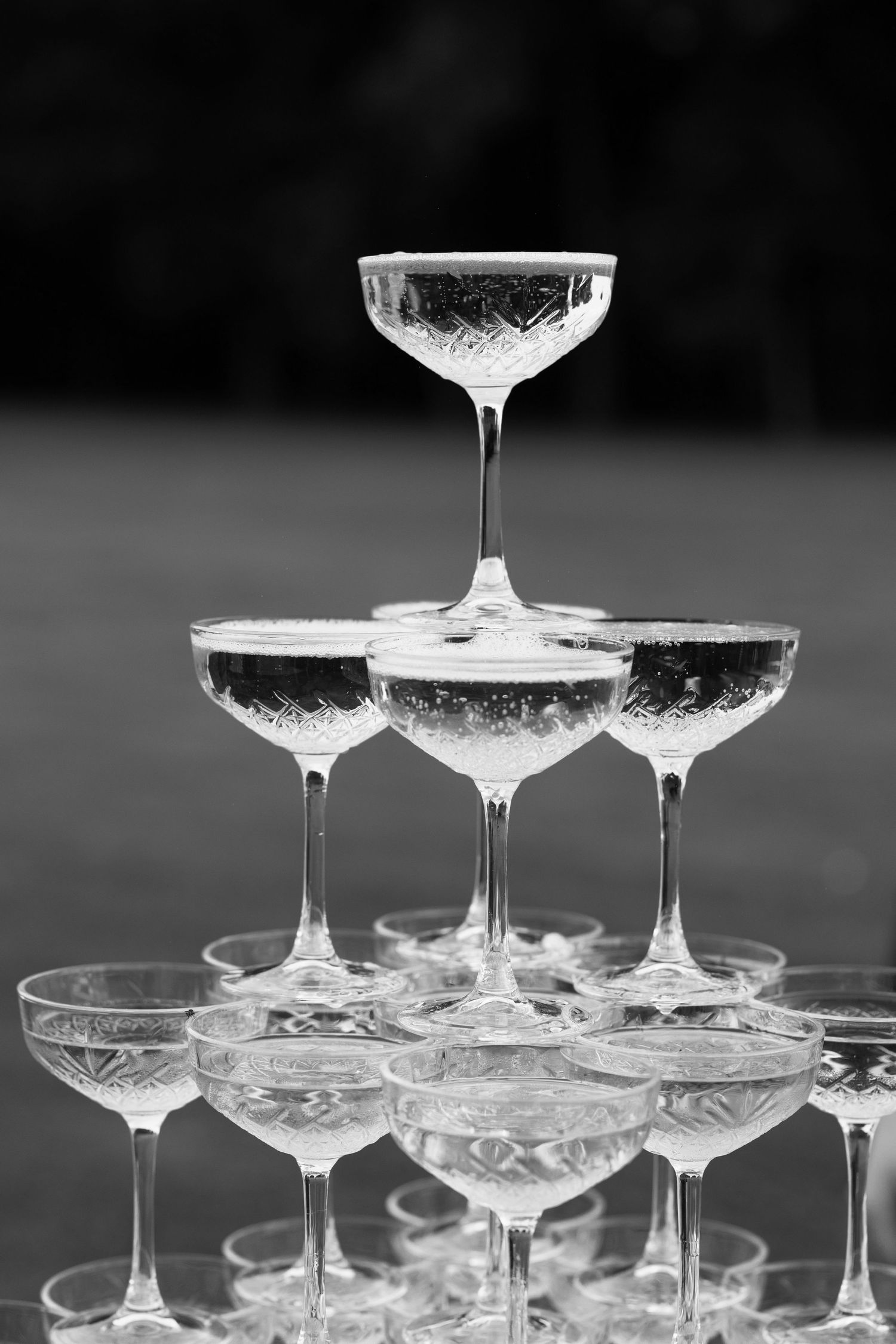 Black and white photo of an elegant champagne glass pyramid tower arrangement at a celebration event.