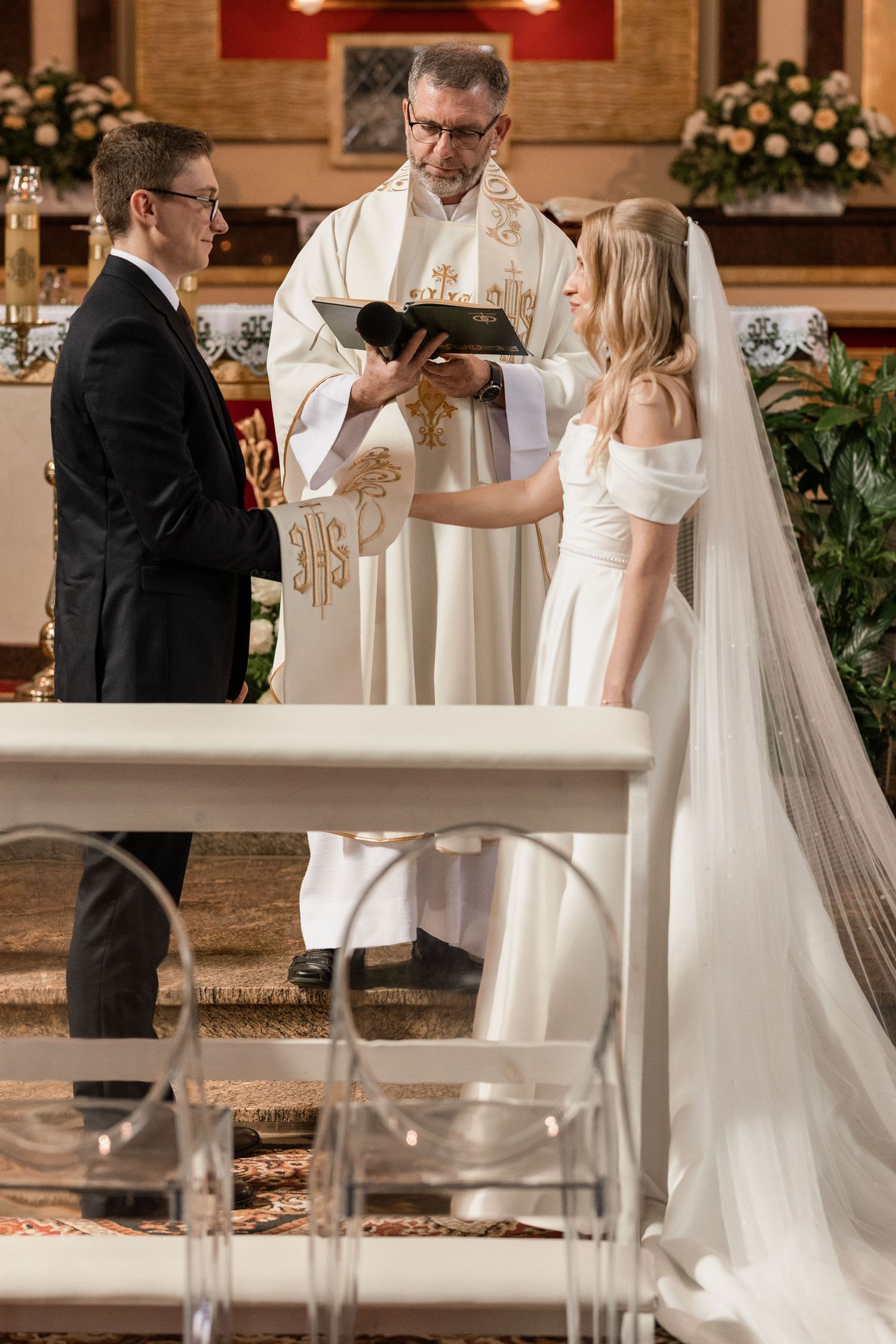 A traditional church wedding ceremony with a priest officiating as a couple exchanges vows at the altar.