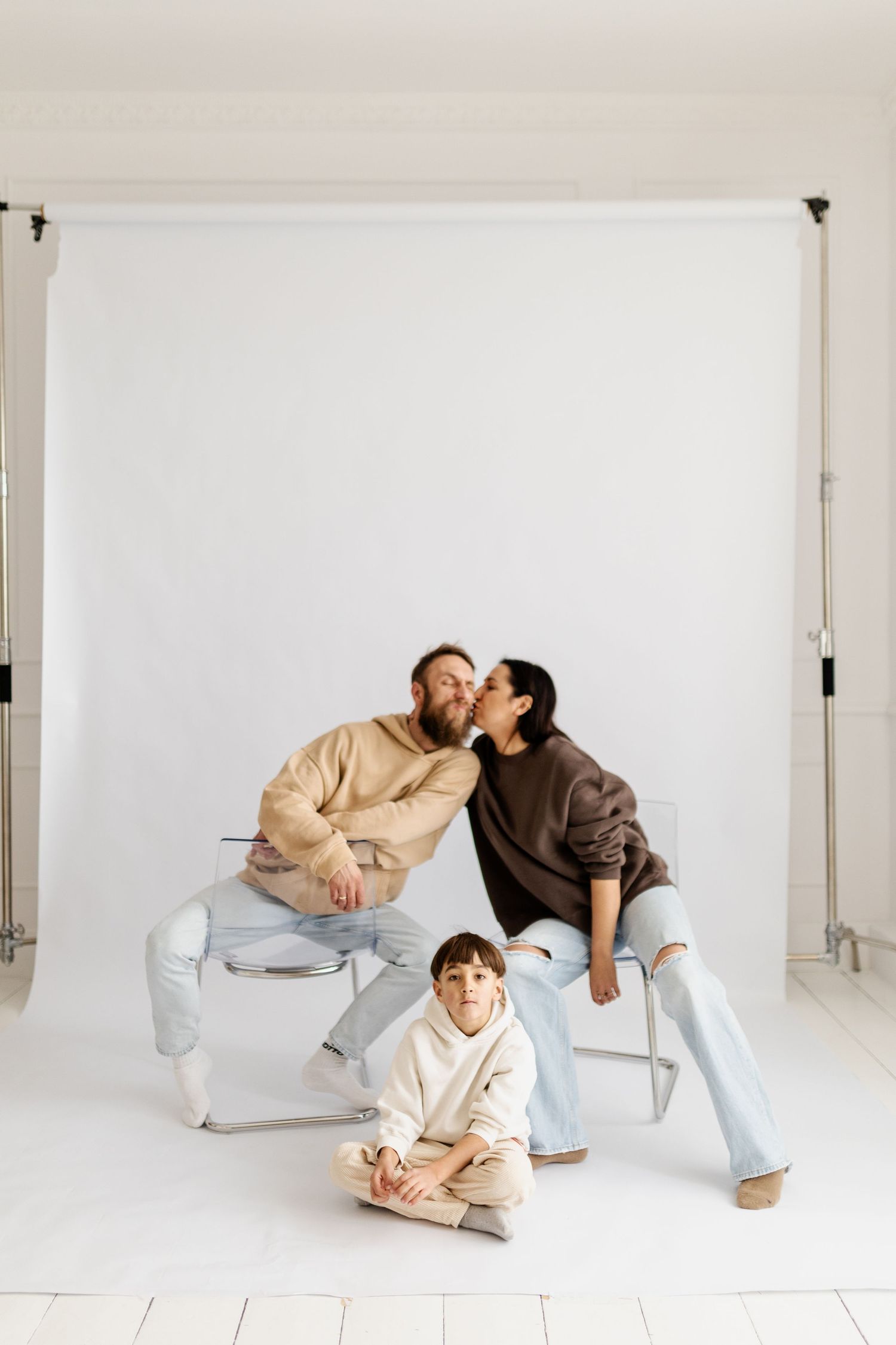 Family portrait in studio with couple and child posed against white backdrop.