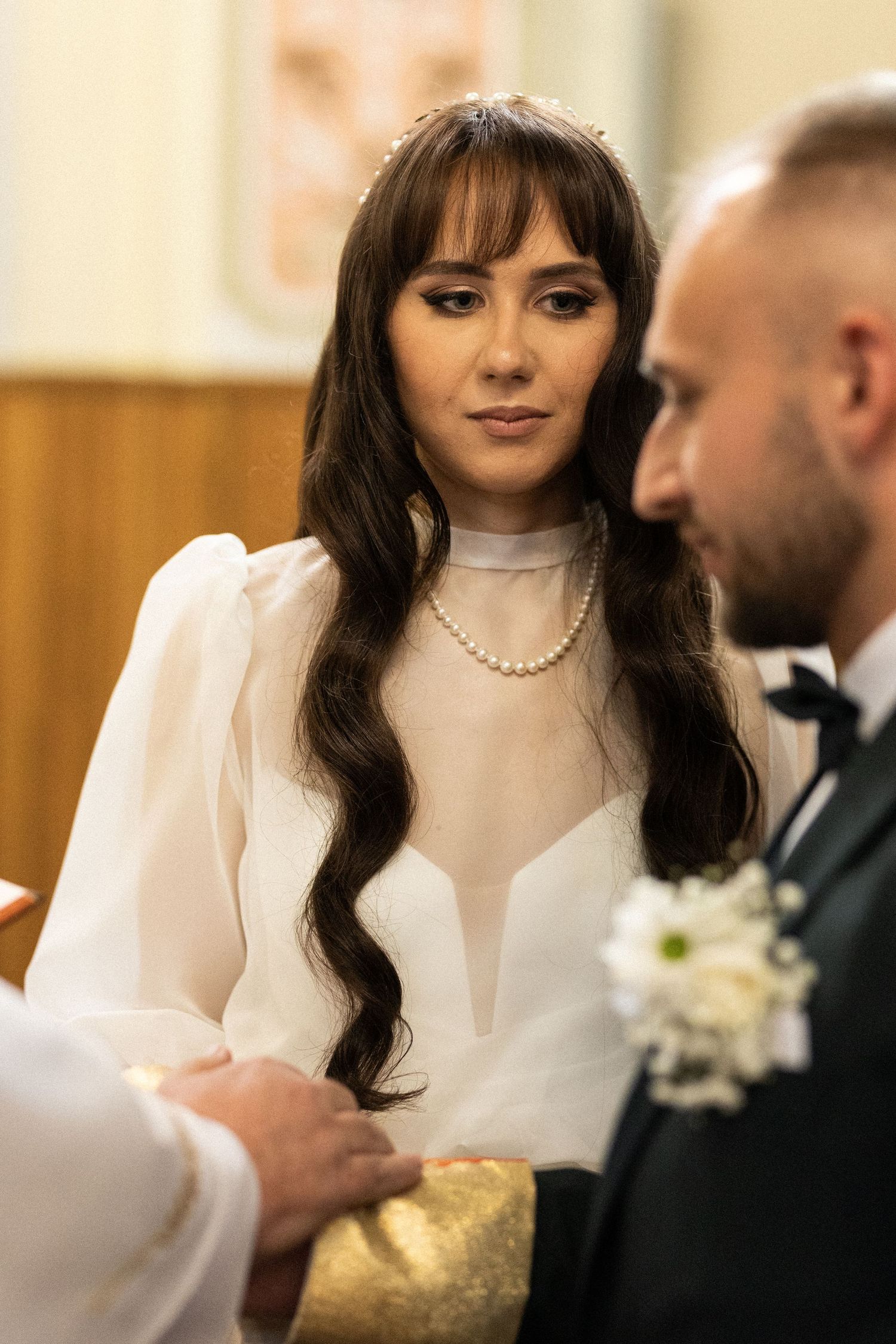 A couple during their wedding ceremony with the bride wearing a white dress with sheer details and pearl necklace.