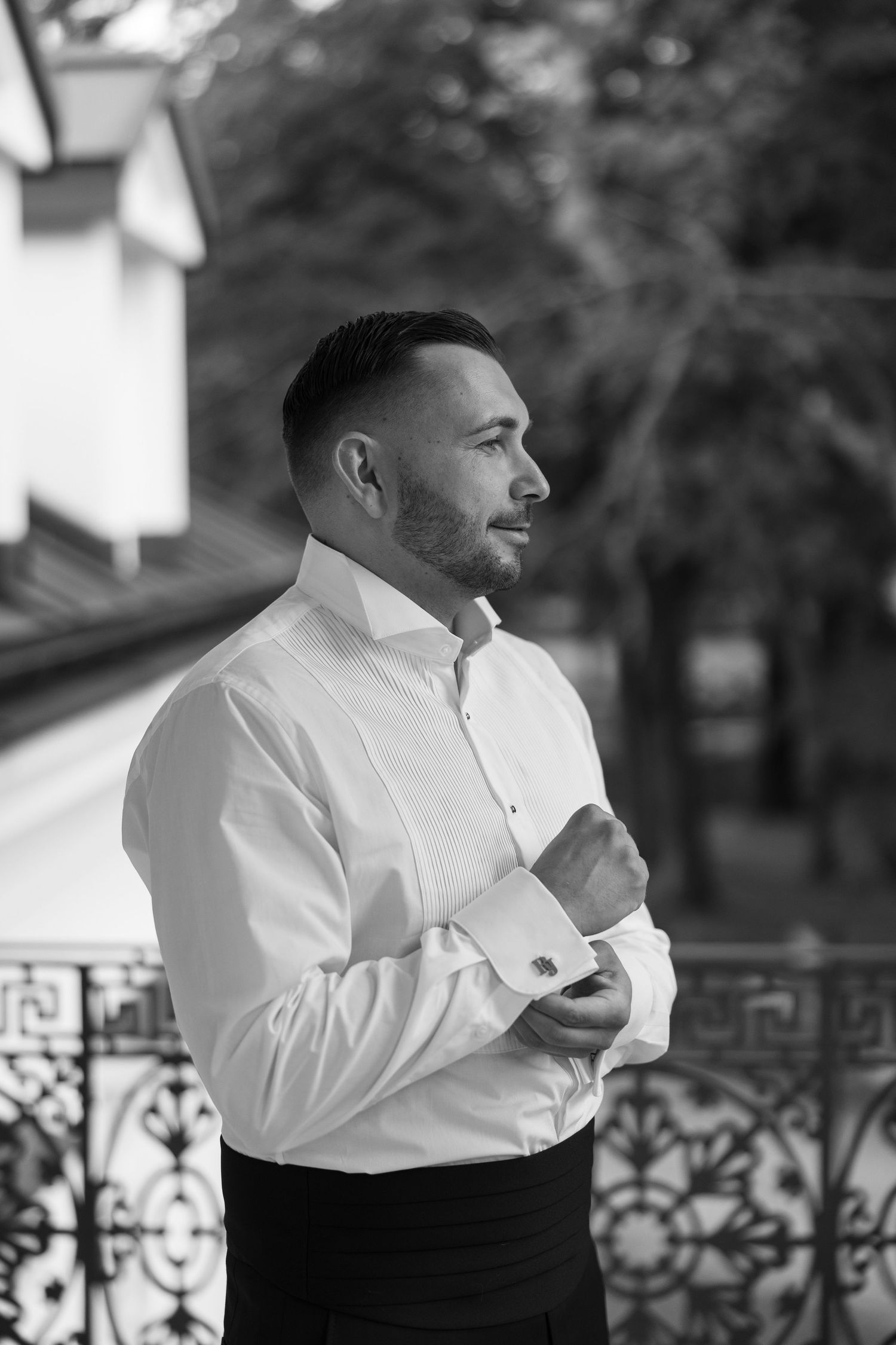 Black and white photo of a well-dressed man in a white dress shirt adjusting his cufflinks on an ornate balcony.