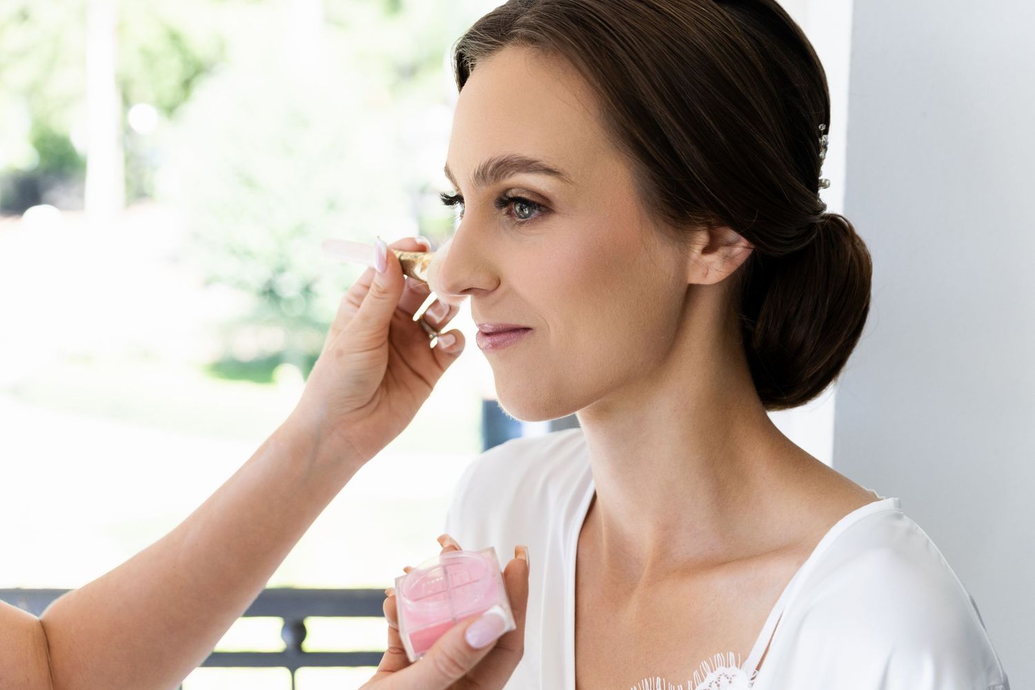 Professional makeup artist applying cosmetics to model in white dress during beauty preparation session.