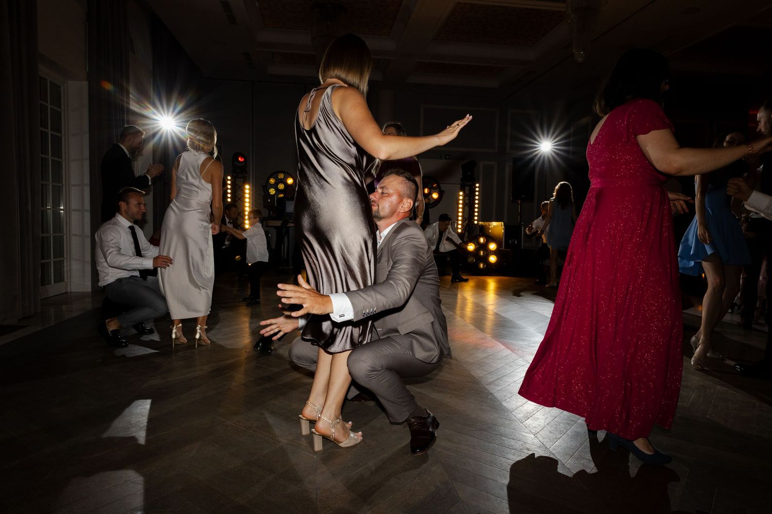 People dancing at an evening event with dramatic lighting as photographers capture the moment on a dark dance floor.