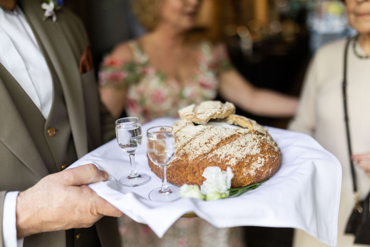 Server carries a rustic loaf of artisanal bread with white garnish on crisp white linen at an upscale event.