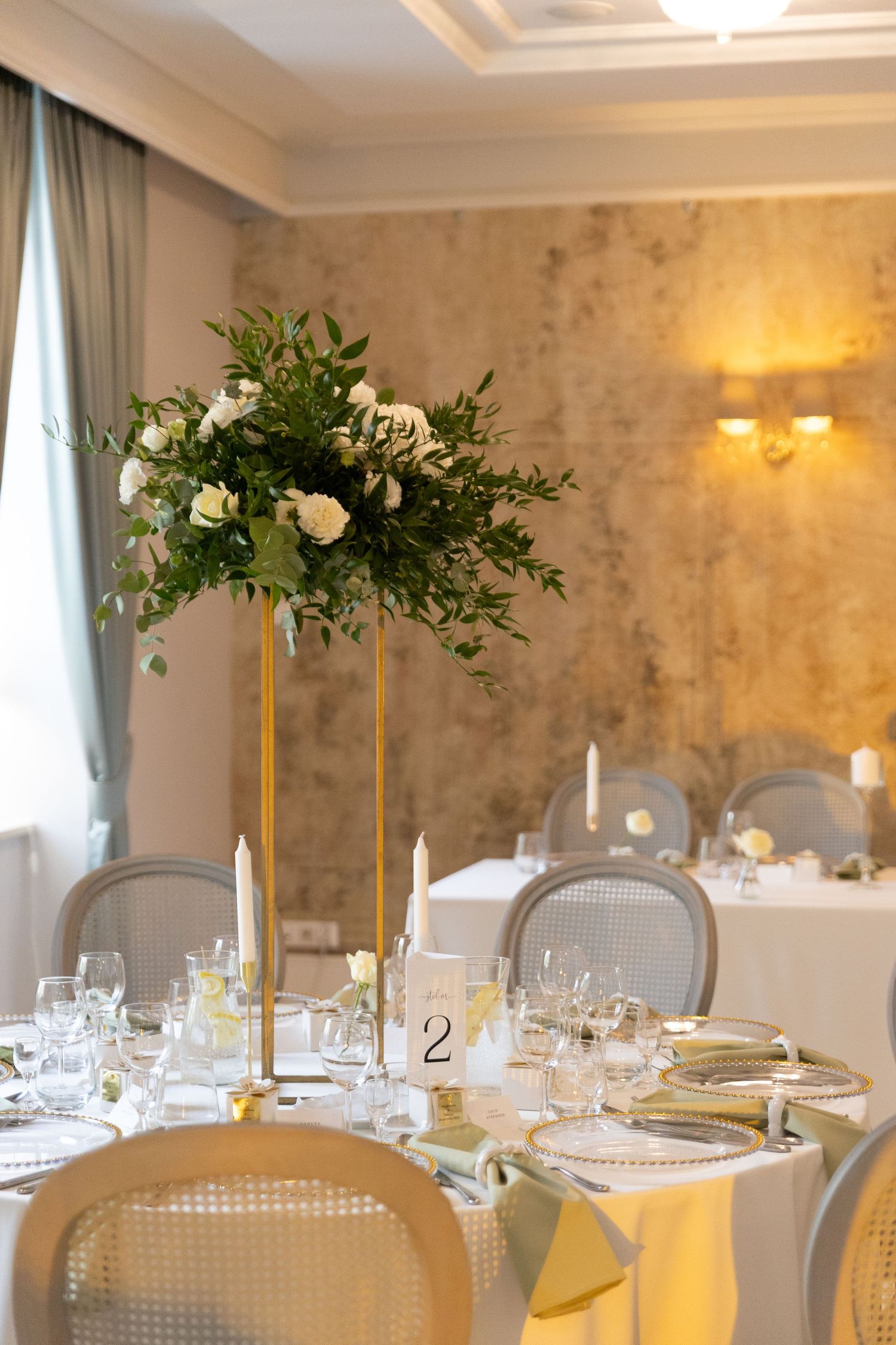 Elegant wedding reception tables with tall gold centerpieces and white floral arrangements in a luxurious ballroom setting.