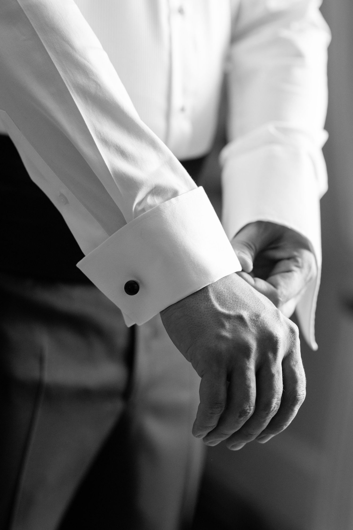 Close-up black and white photo of hands adjusting white shirt cuffs in a formal setting.
