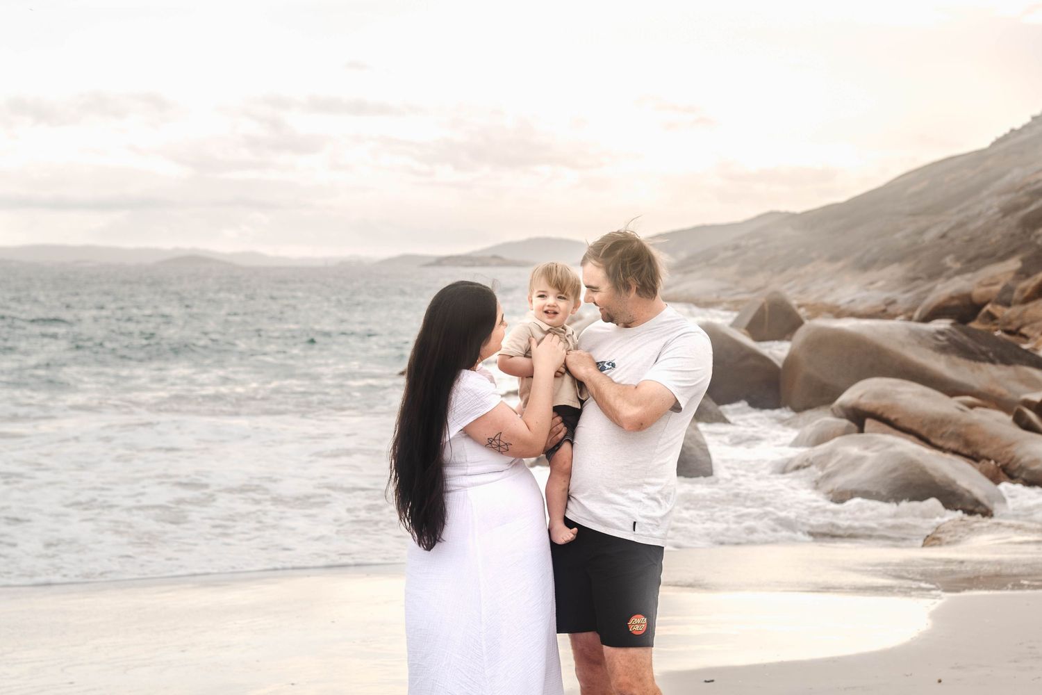 Loving family moment captured on a scenic beach with rocky coastline.