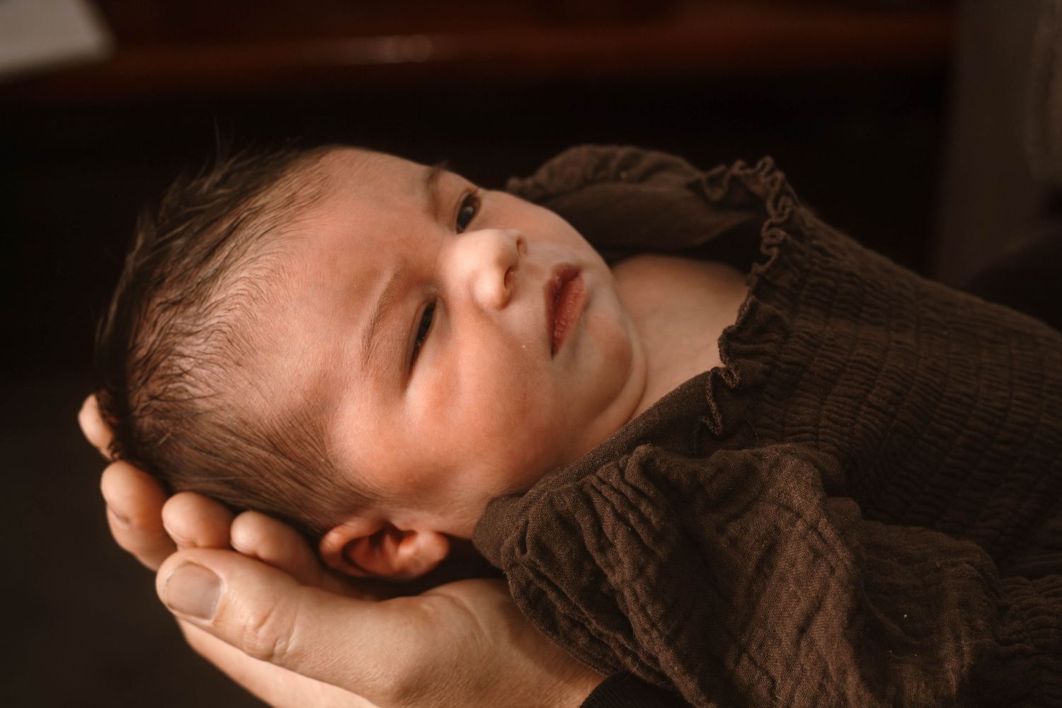 Profile view of a sleeping newborn baby cradled in gentle hands.