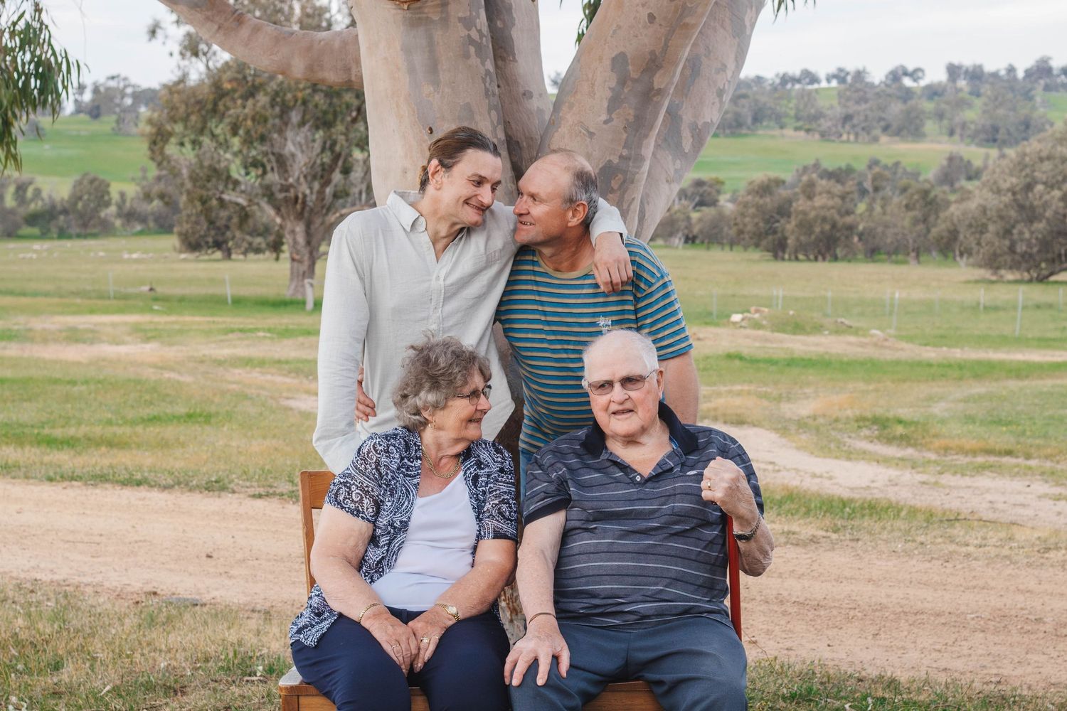 Family members sharing warm moments together while seated under large gum tree.