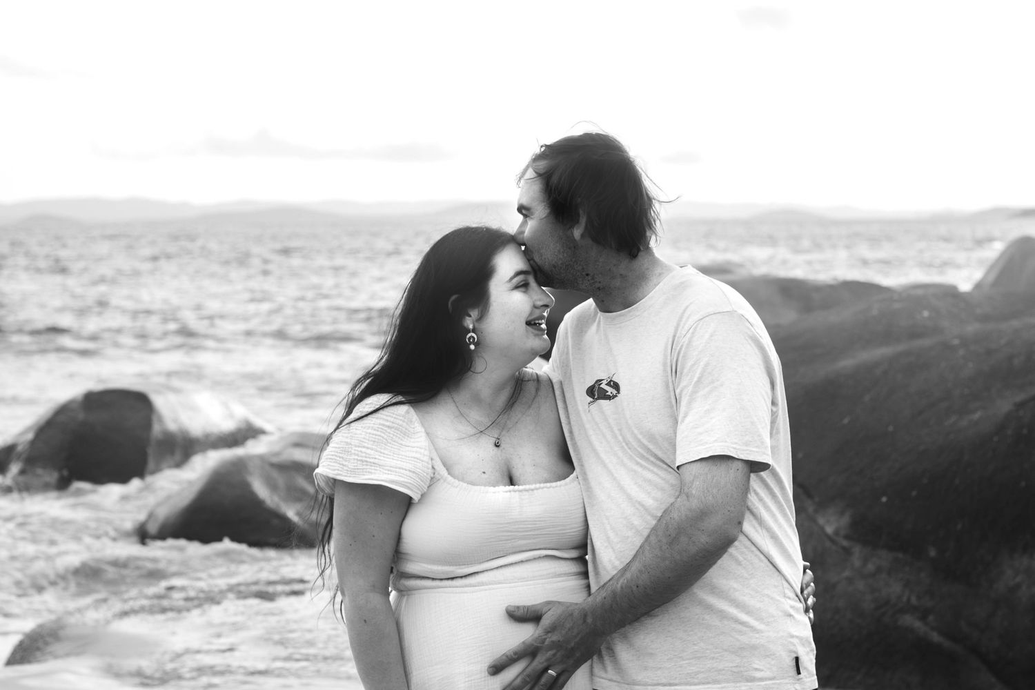 Black and white portrait of a couple embracing on a rocky shoreline.