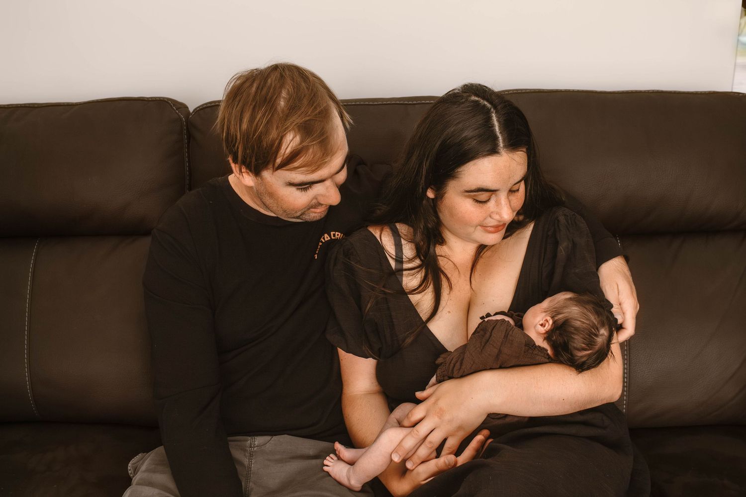 Couple on leather couch gazing lovingly at their newborn baby.