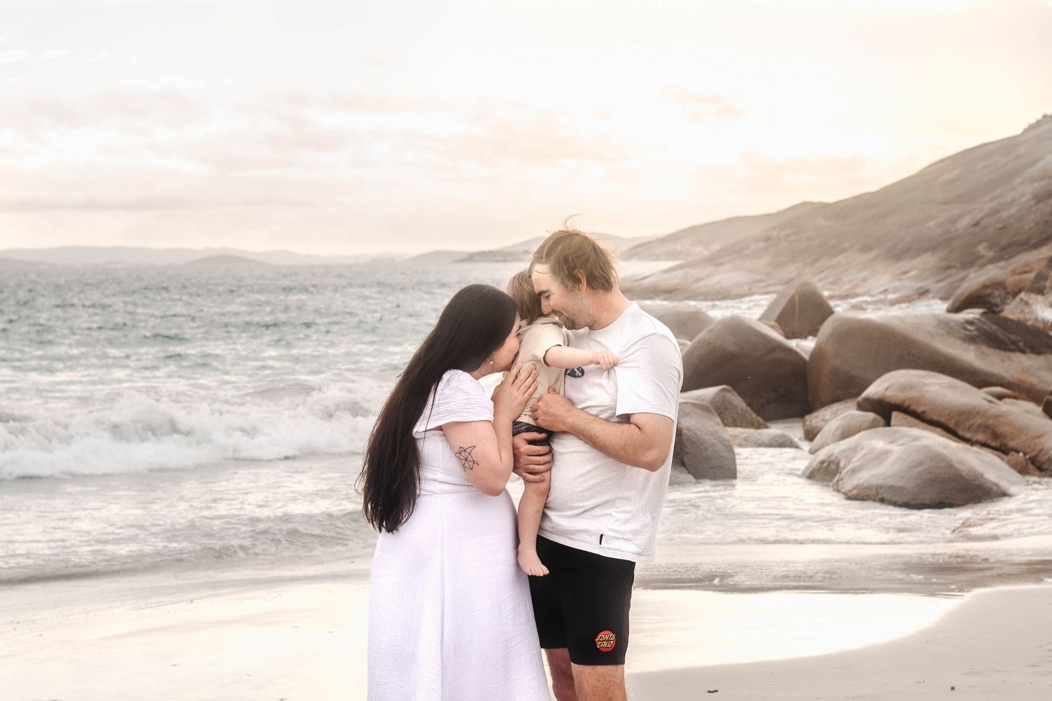 Intimate family moment at sunset on a rocky beach with ocean waves in the background.