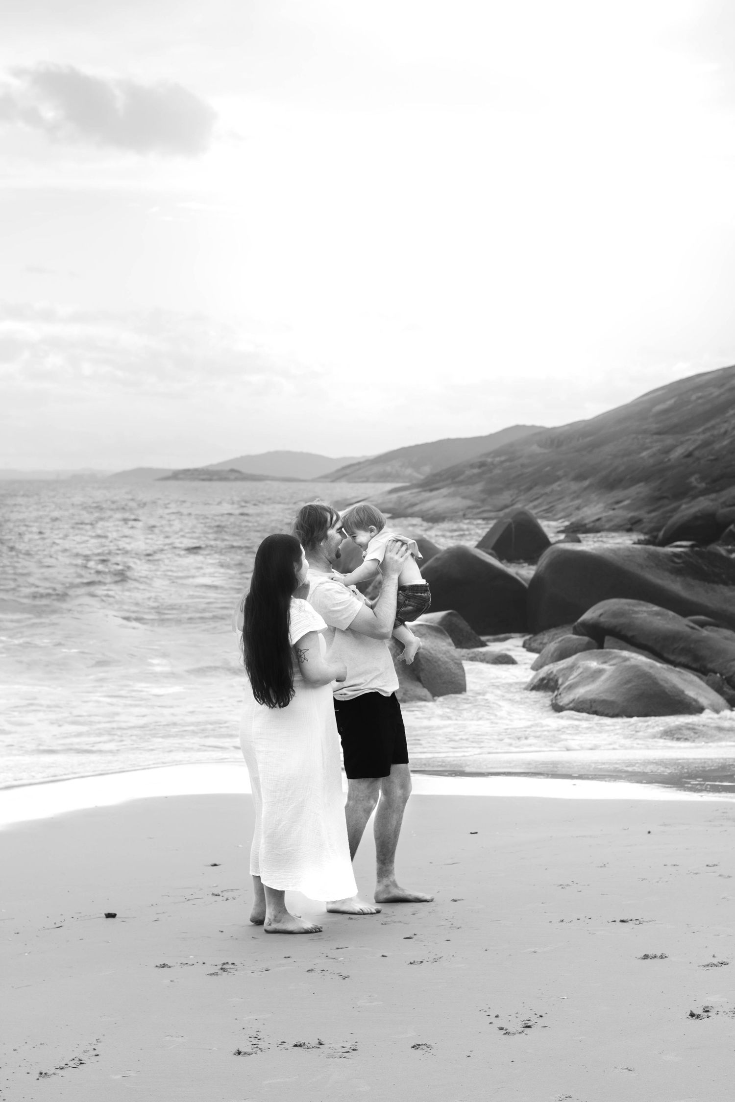 Dancing silhouettes against a misty beach landscape with large rocks and mountains in the background.