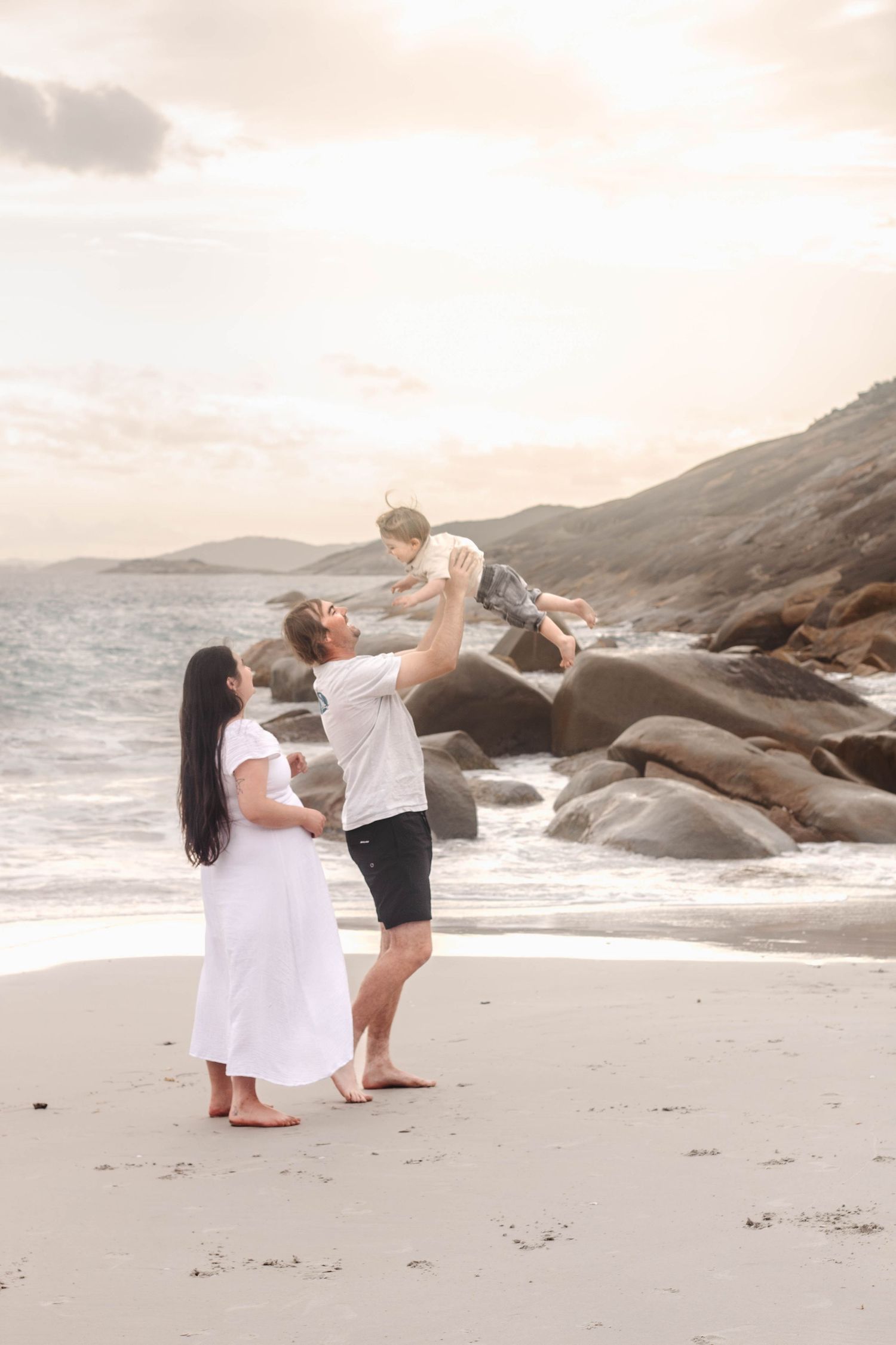 Two people engage in playful dance moves near ocean waves and rocky shoreline.