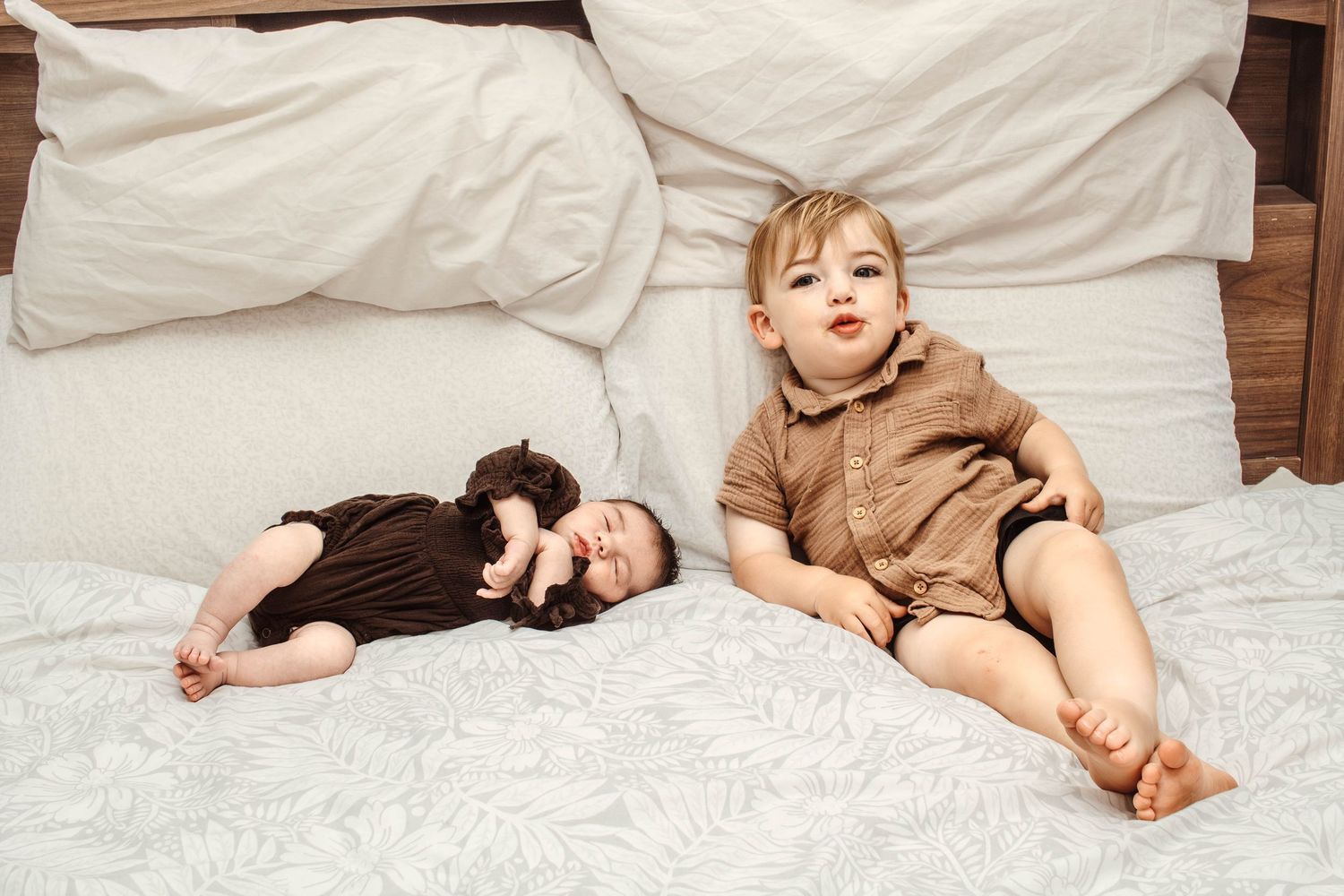 Playful moment captured on white bedding with wooden background.