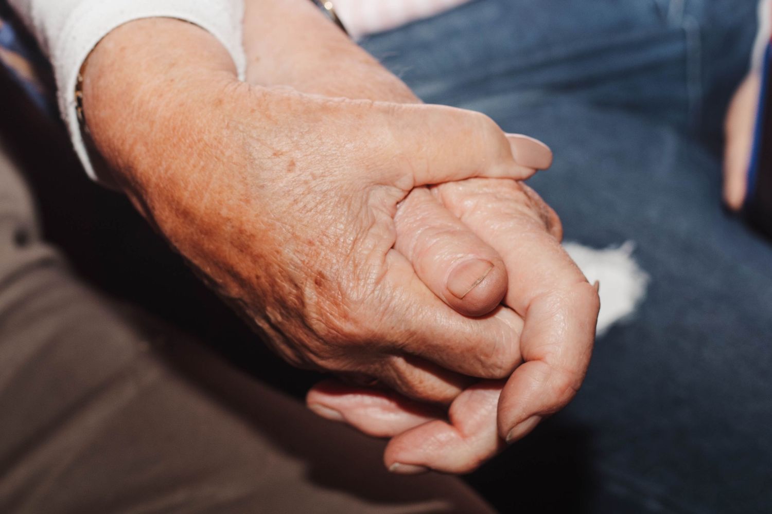 Two weathered hands clasped together in an intimate gesture against a dark background.