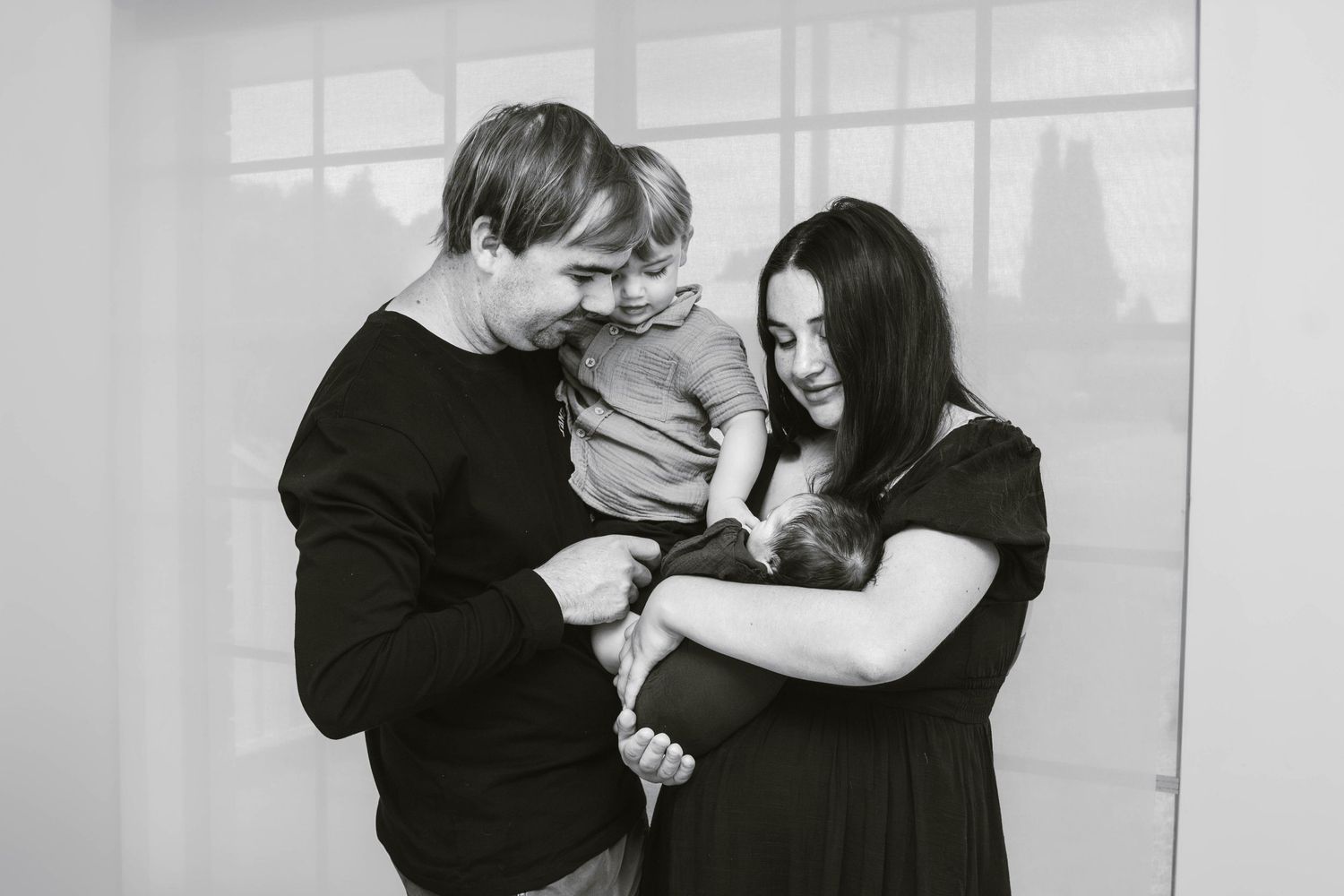Black and white portrait of parents sharing a tender moment with their young child.