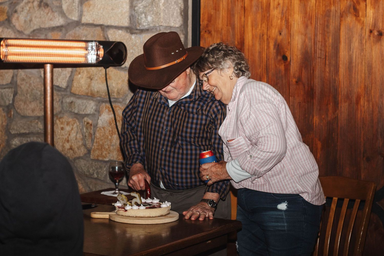 Two people sharing cake and laughter at a wooden table in a rustic setting.