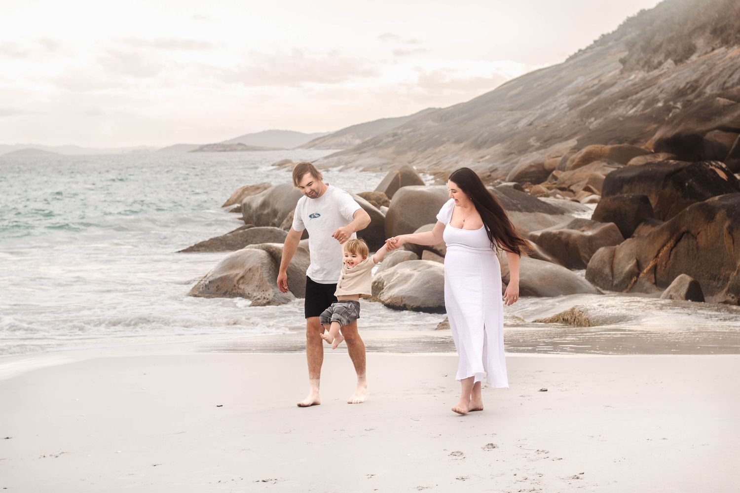 A family plays together on a pristine beach with dramatic coastal rocks.