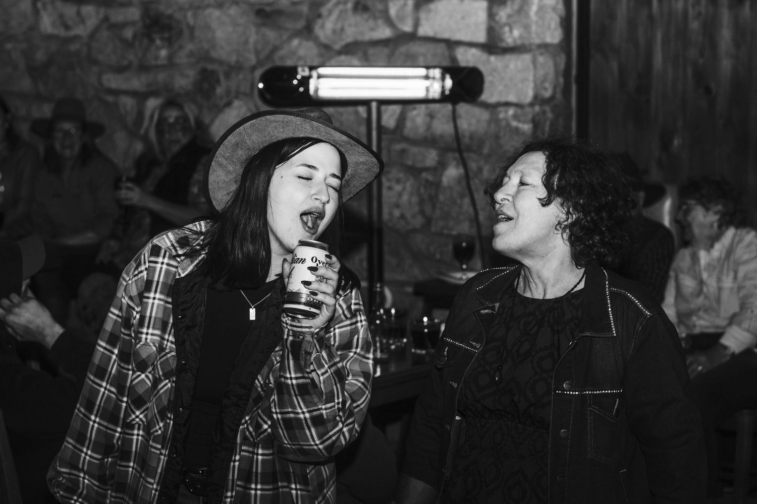 People at a social gathering are laughing while wearing plaid flannel shirts in a dimly lit space.