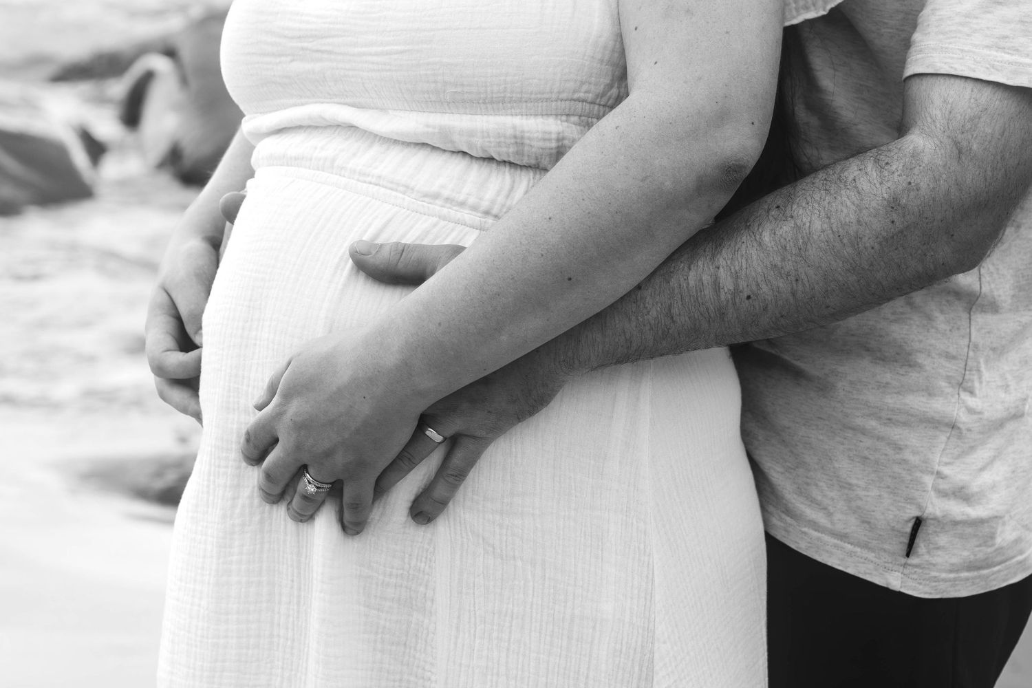 Black and white detail shot of hands tenderly holding pregnant belly.