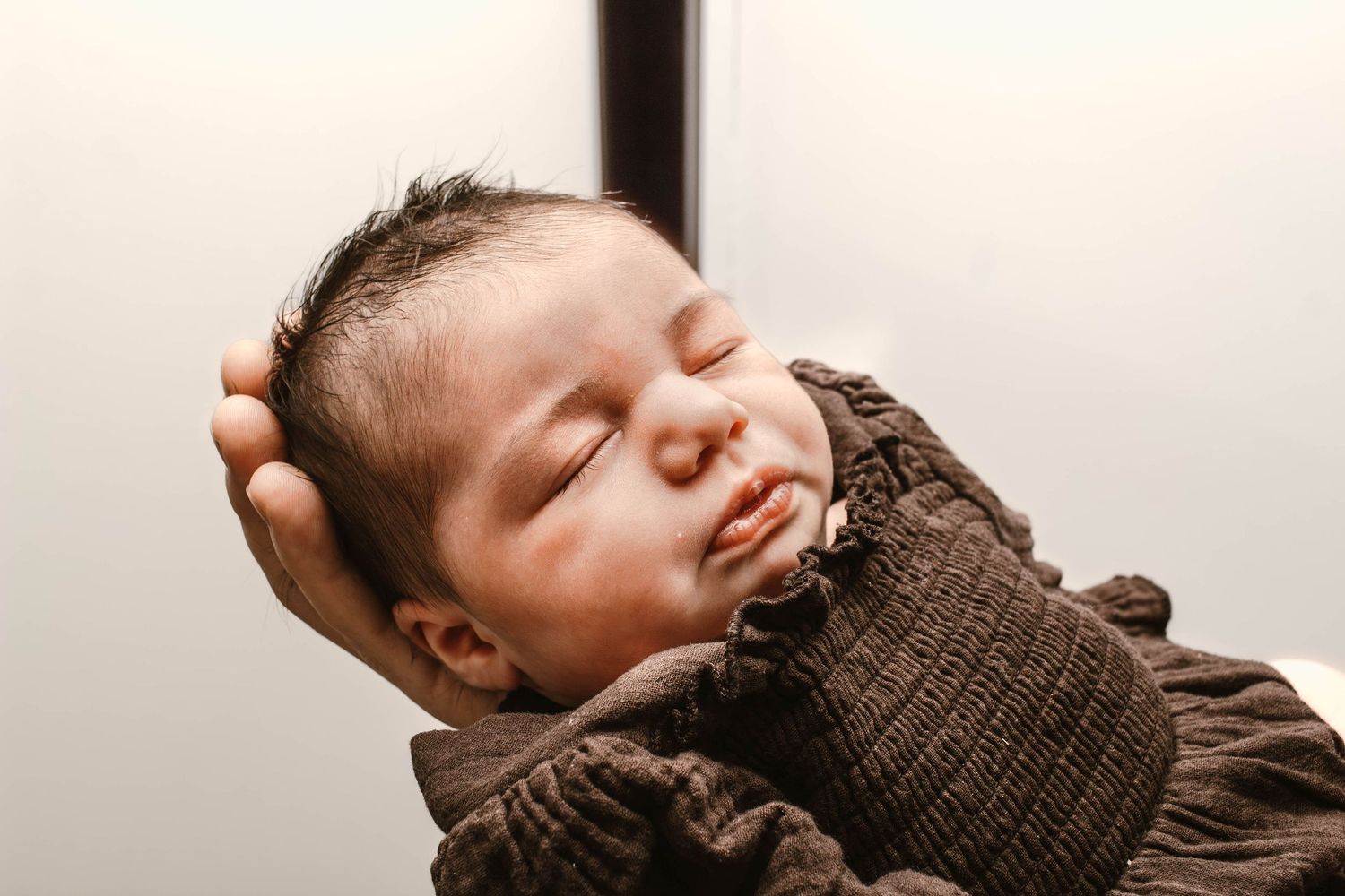 A sleeping newborn baby wearing a brown knit sweater rests peacefully.