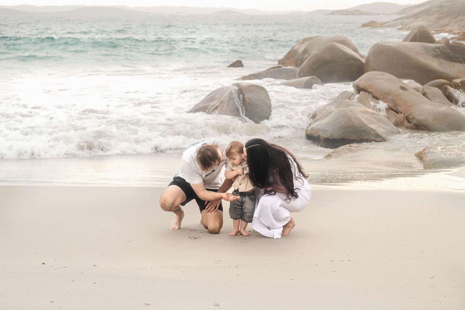 Family enjoying moment together on scenic beach with rocky outcrops.