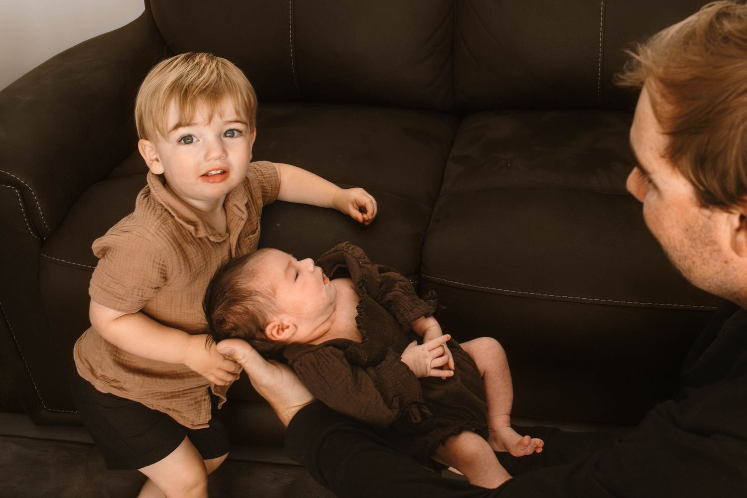 Two children playing on a dark leather couch during a family photo session.