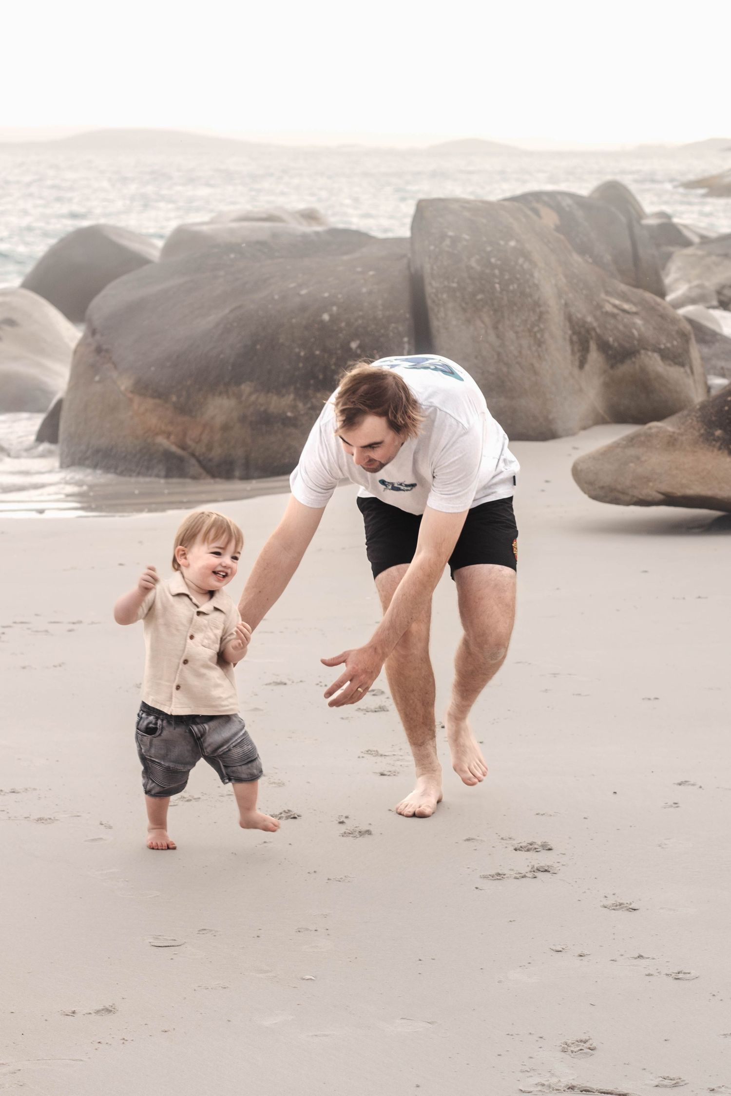 A tender moment between parent and toddler playing together on a rocky beach at sunset.