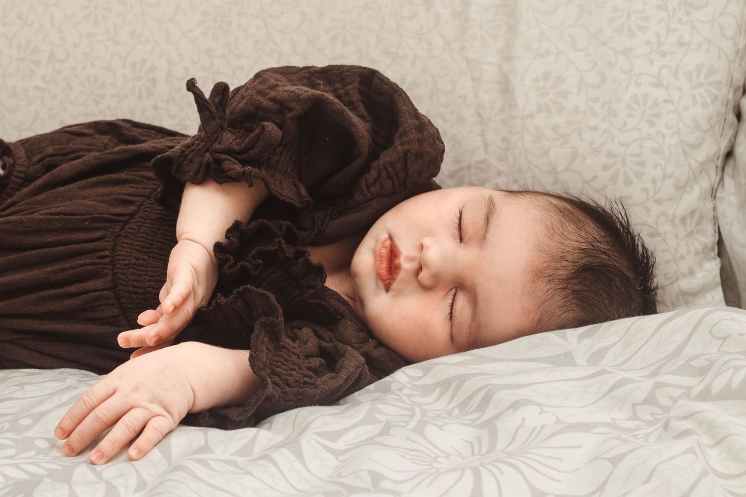 Infant napping in vintage-style brown dress on cream colored pillow.