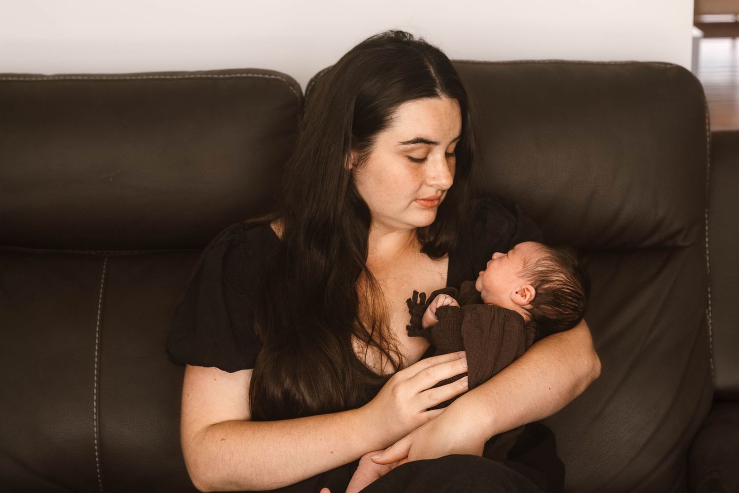 A tender moment of parent and newborn resting together on a brown leather couch.
