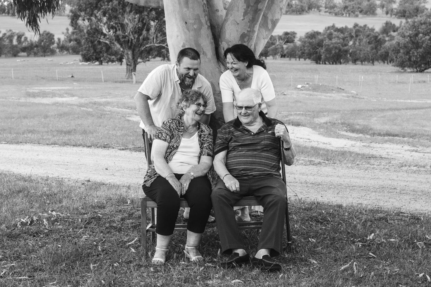 Black and white portrait of family gathering under eucalyptus tree in rural setting.