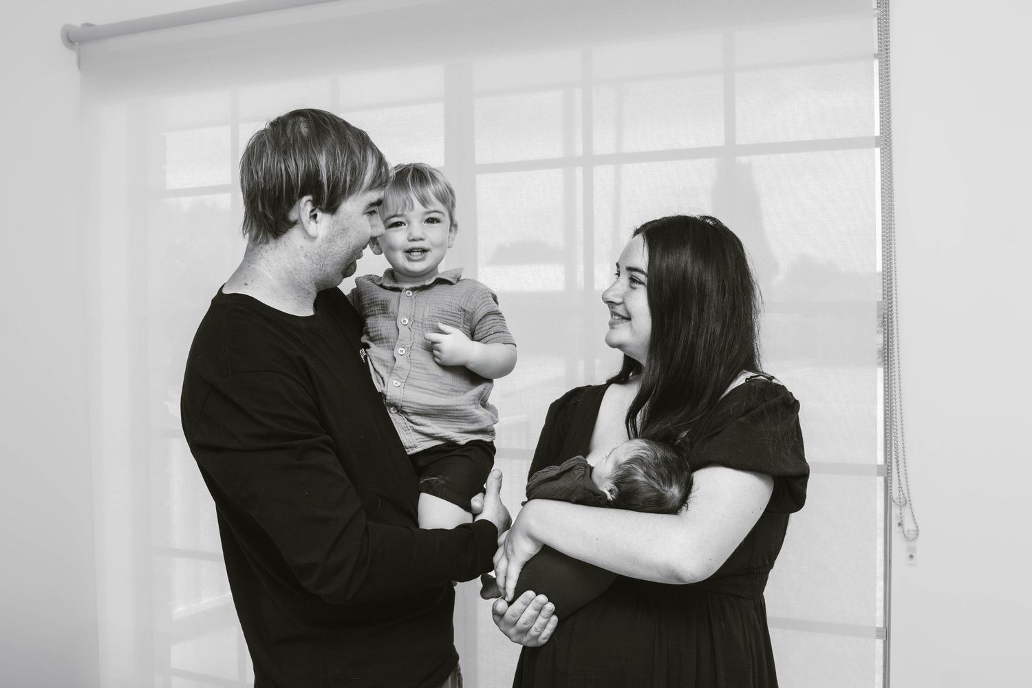 Candid black and white photo of parents laughing with their energetic toddler.