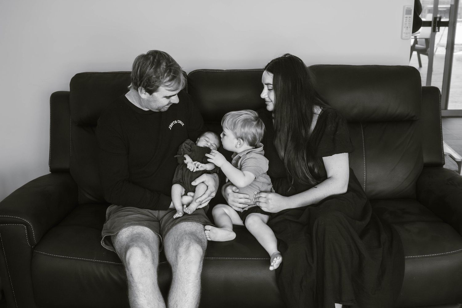 Family relaxing together on a black leather couch in black and white.