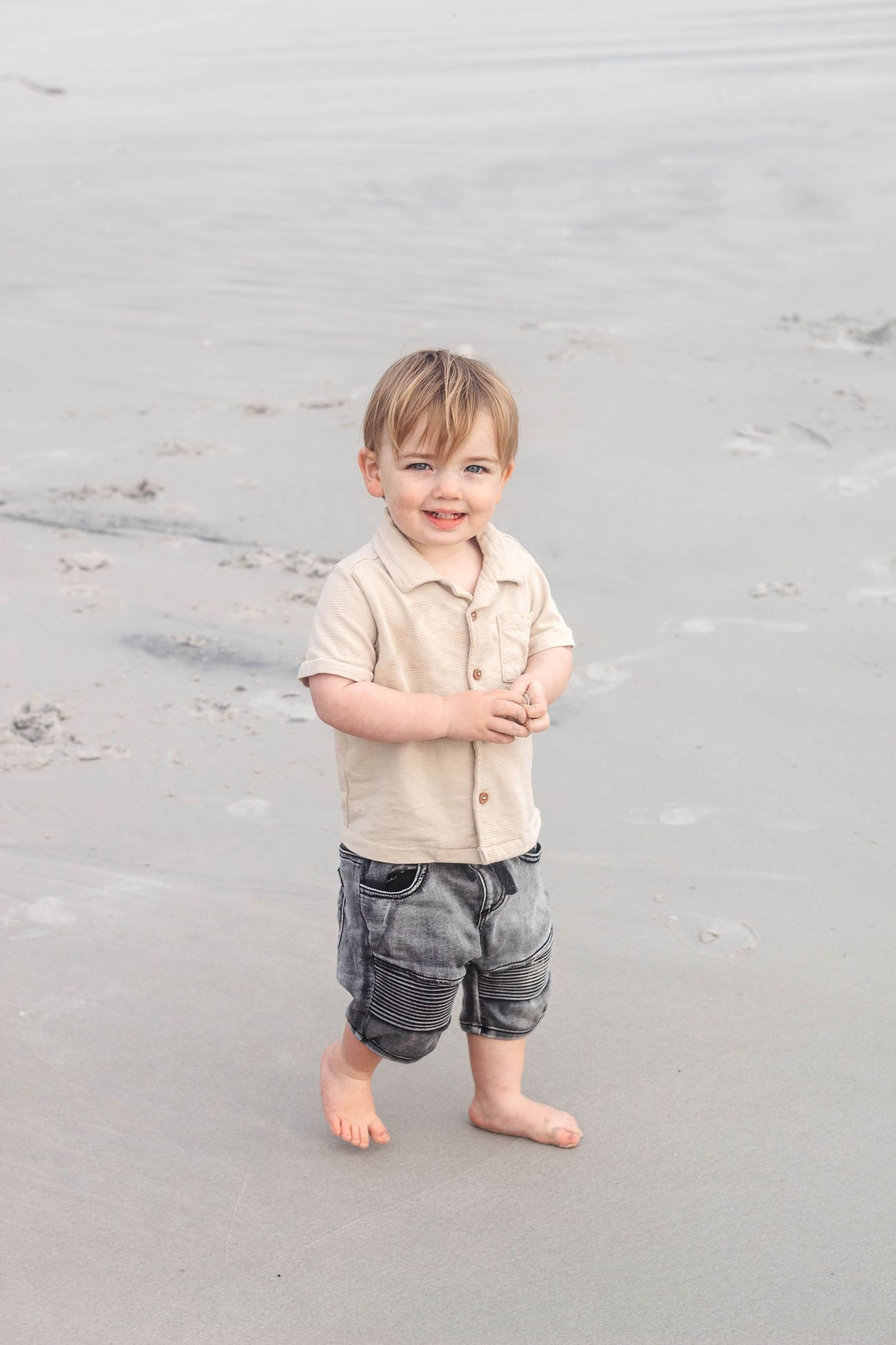 Small child walking barefoot on grey sand during a beach photoshoot.