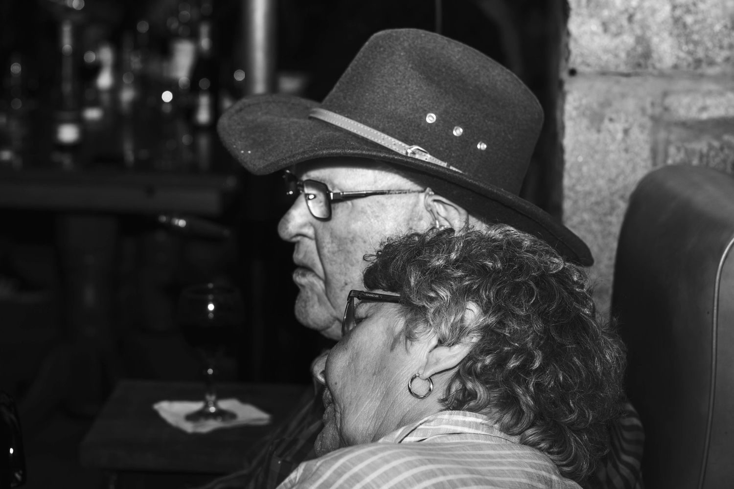 Profile view of person wearing glasses and black hat in dim lighting.