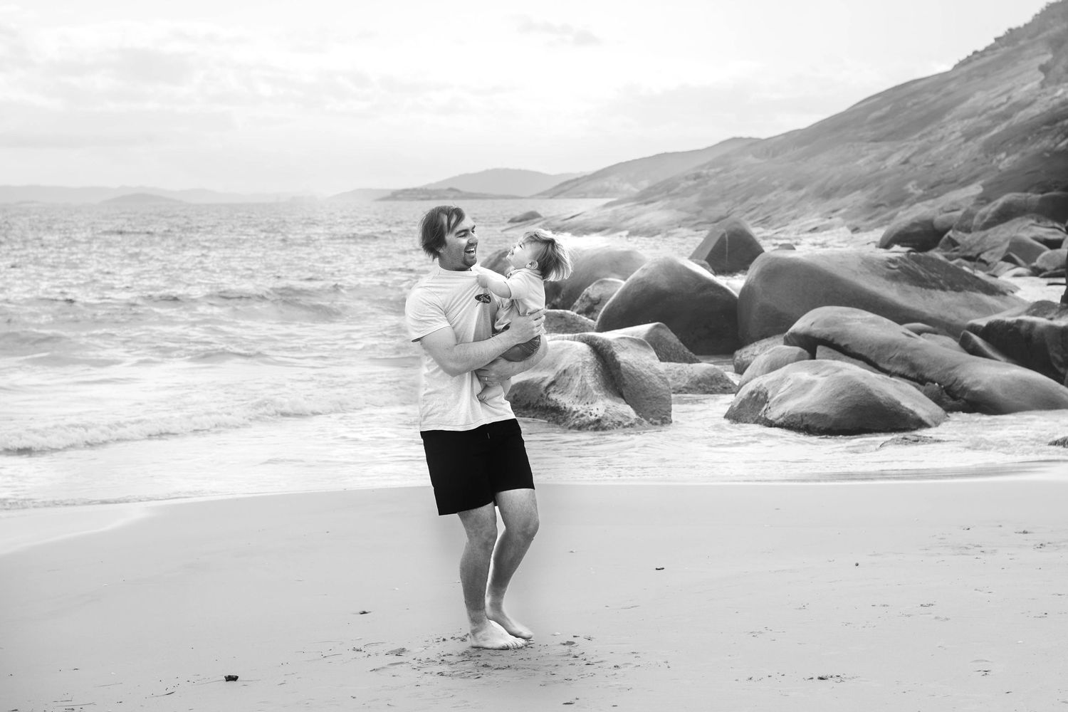 Dynamic dance poses photographed on a serene beach with dramatic rocky landscape.