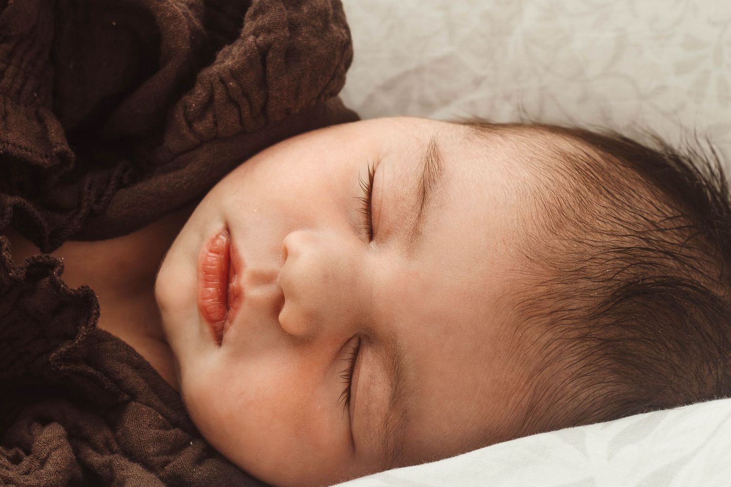 Sleeping infant in brown dress resting peacefully on white pillow.