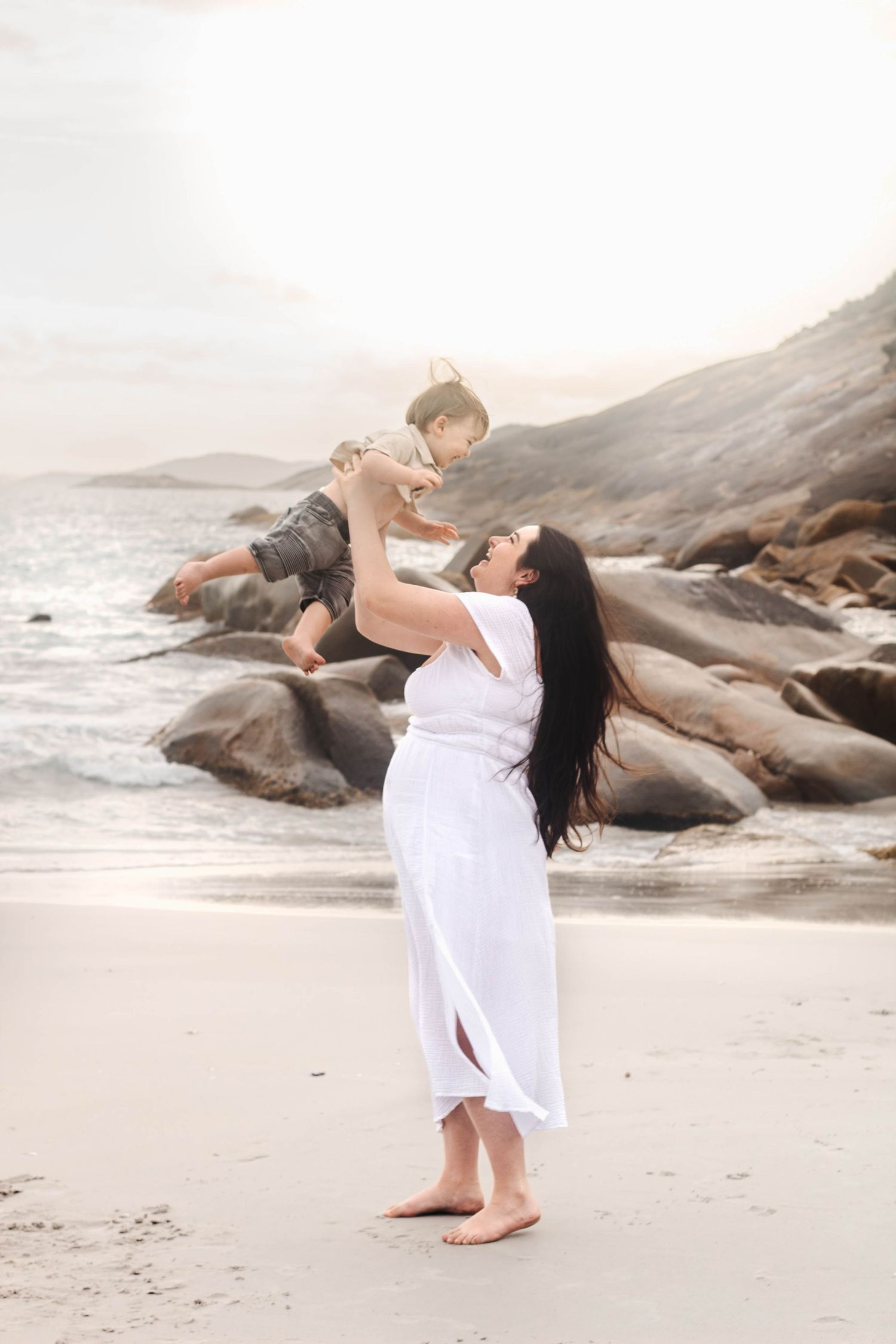 Graceful dance lifts performed on a tranquil beach with mountains and rocks in the background.