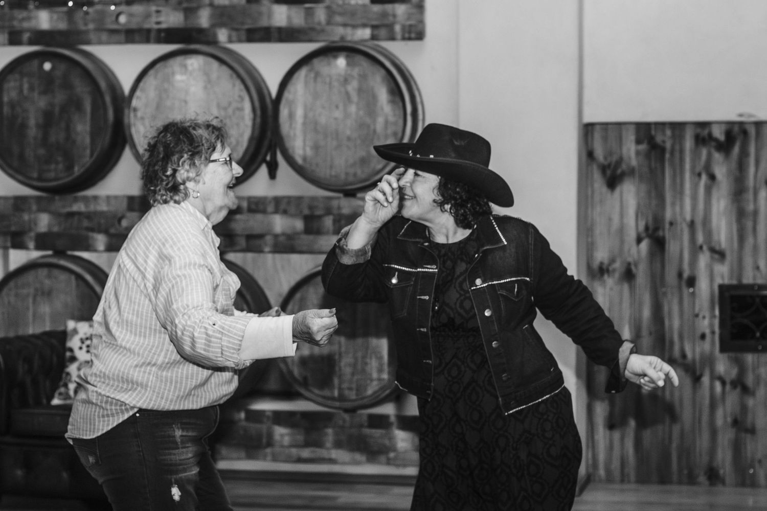 Two people dancing energetically in front of wine barrels in black and white.