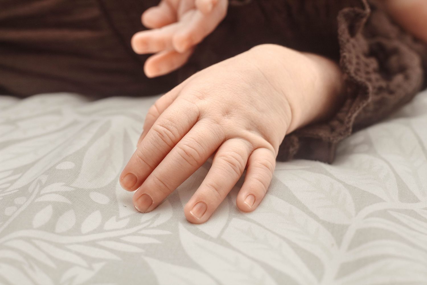Small delicate hand of baby resting on white textured bedding.