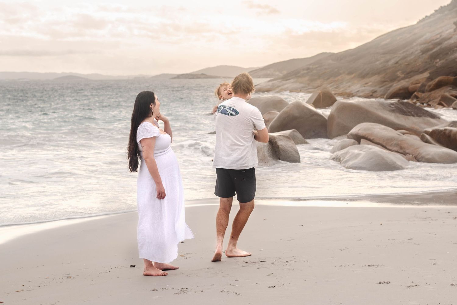 Dancers perform graceful movements on a peaceful beach with mountainous backdrop.
