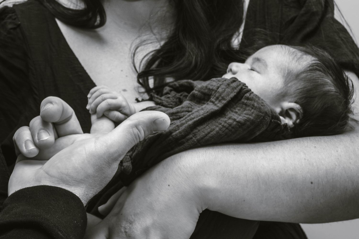 Black and white close-up of hands tenderly holding a sleeping infant.