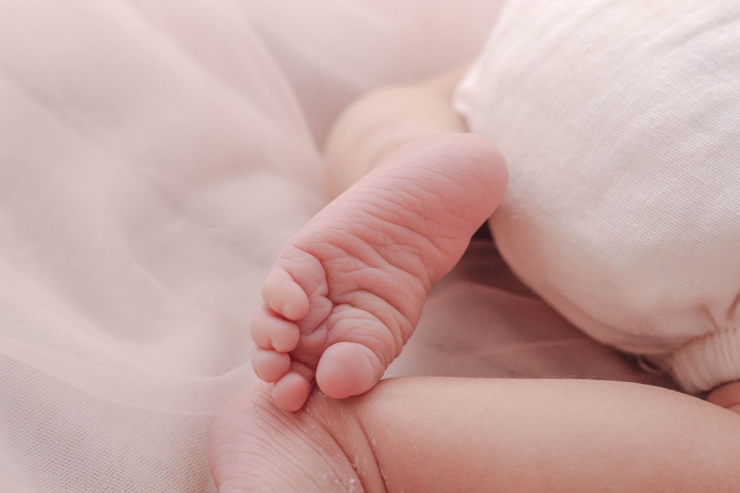 Close up of a tiny baby foot wrapped in soft pink blankets showing delicate toes and skin texture.