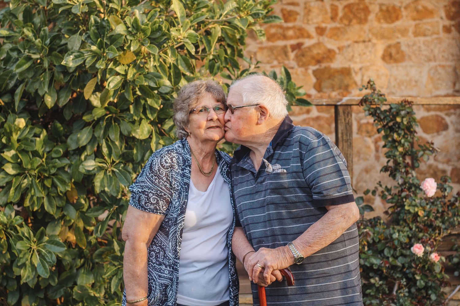 Intimate moment between senior couple against stone wall with climbing plants.