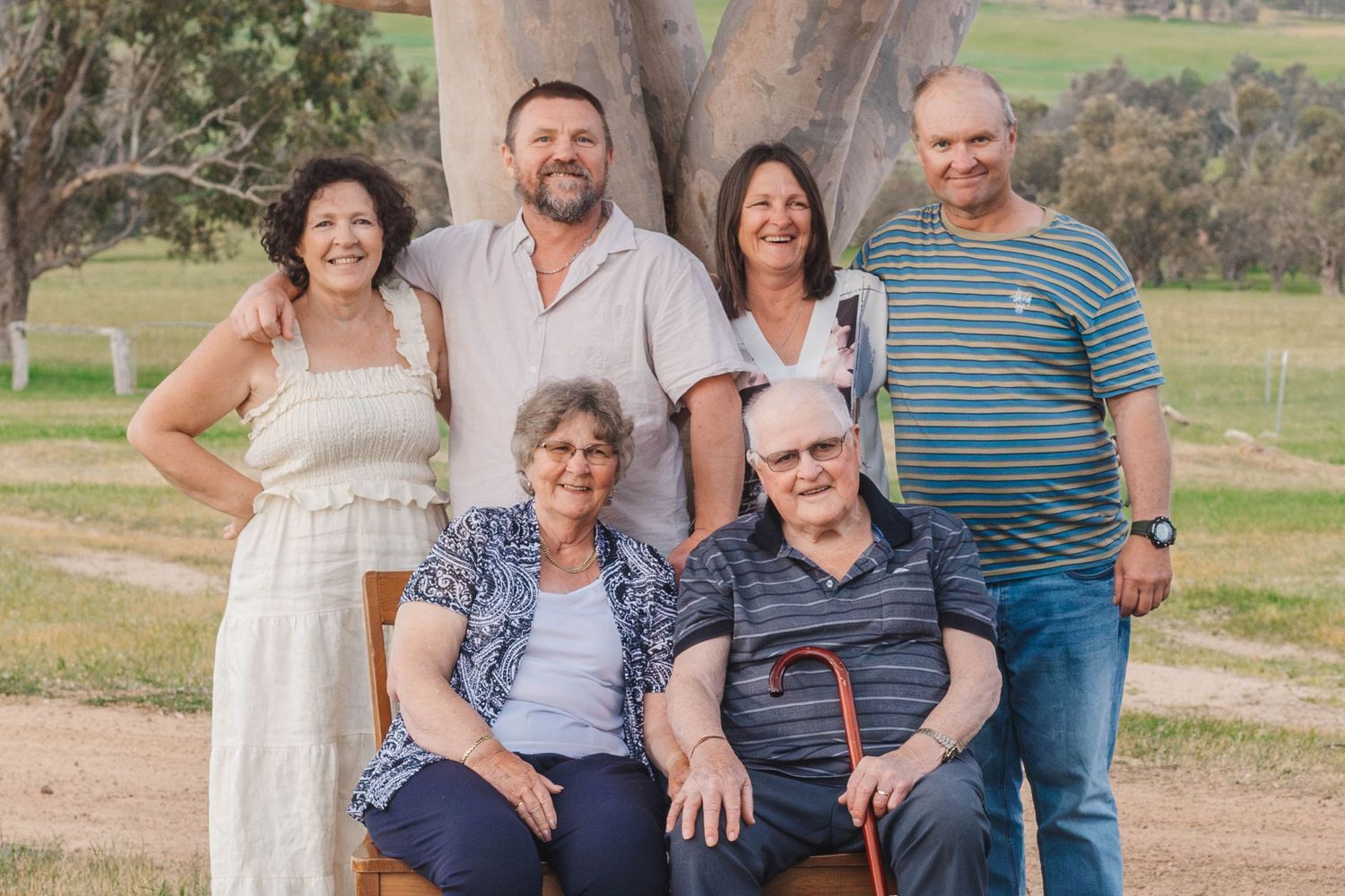 Casual family gathering outdoors with three generations smiling together against a rural backdrop.