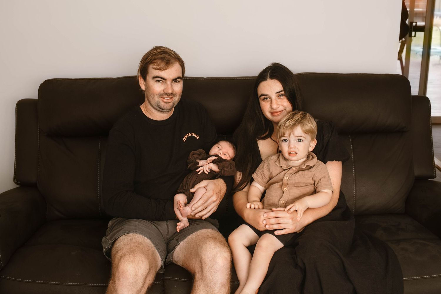 Casual family portrait on a brown leather couch in warm tones.