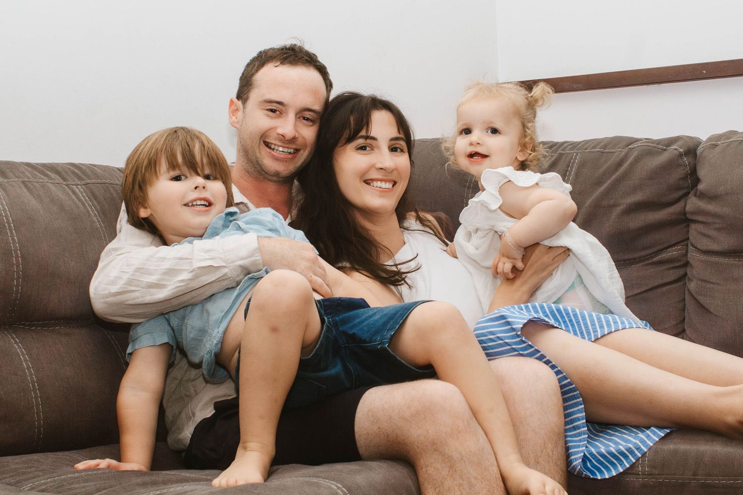A smiling family relaxes together on a brown couch in their living room.