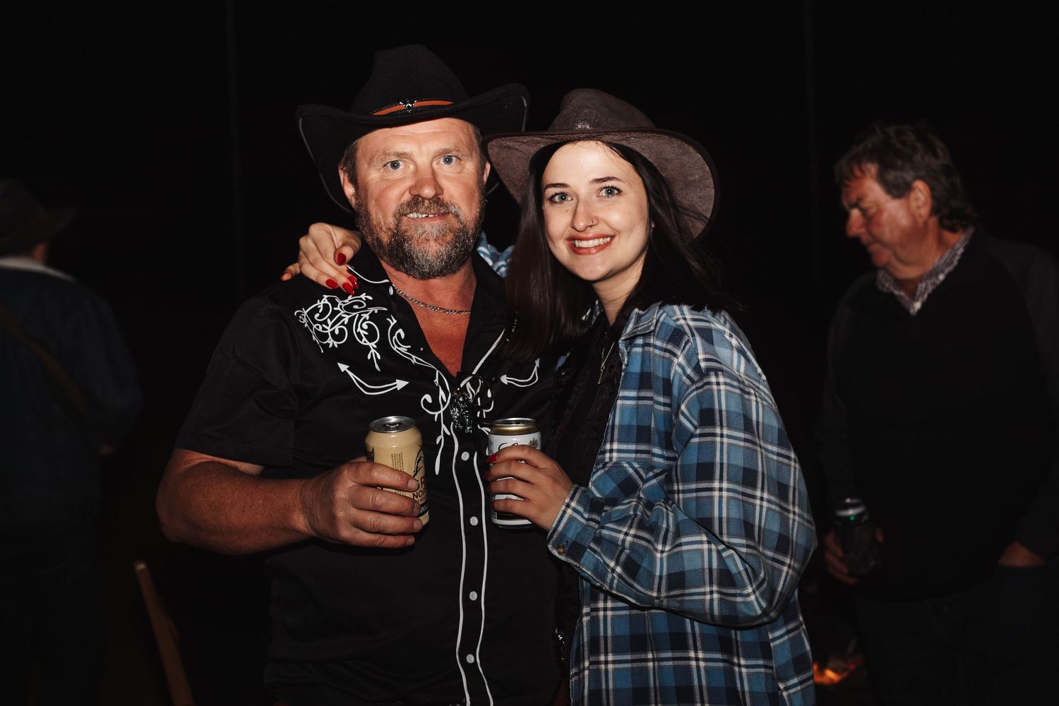 Two people in western attire sharing drinks and smiles at a dimly lit gathering.